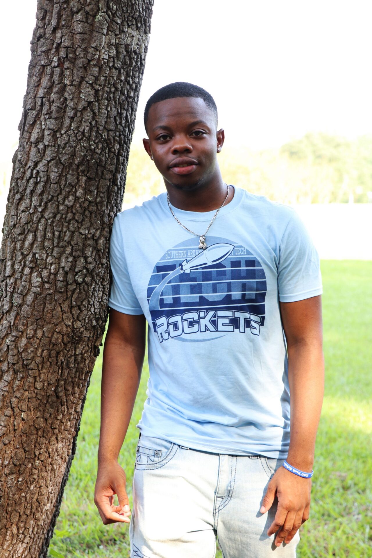 young man in blue t-shirt leaning against a tree