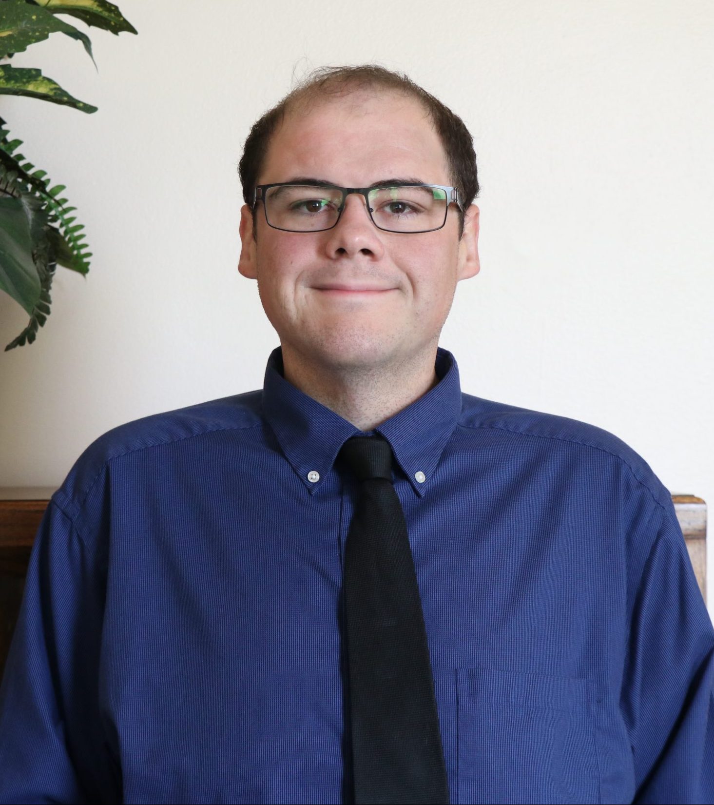 man wearing blue shirt and black tie smiling