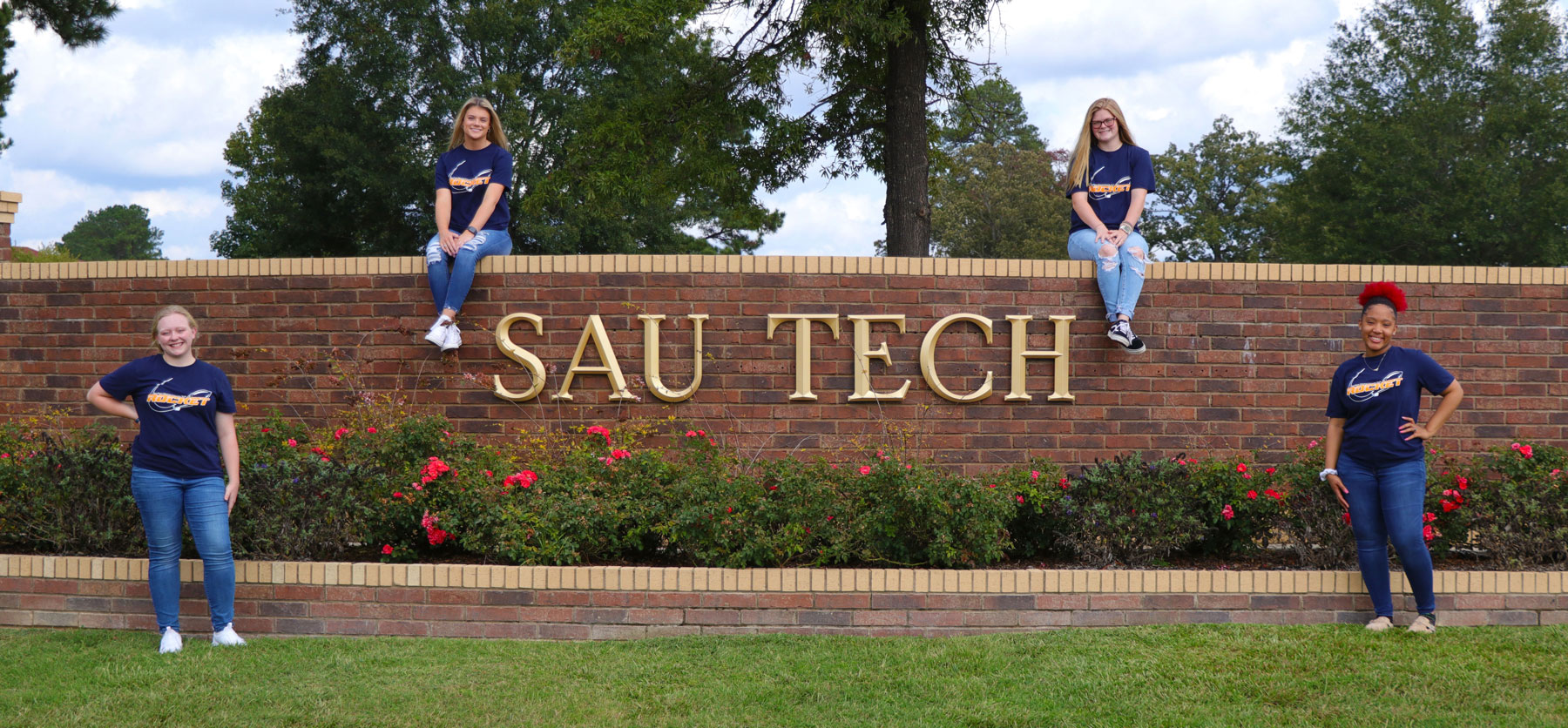 college students sitting on a brick sign